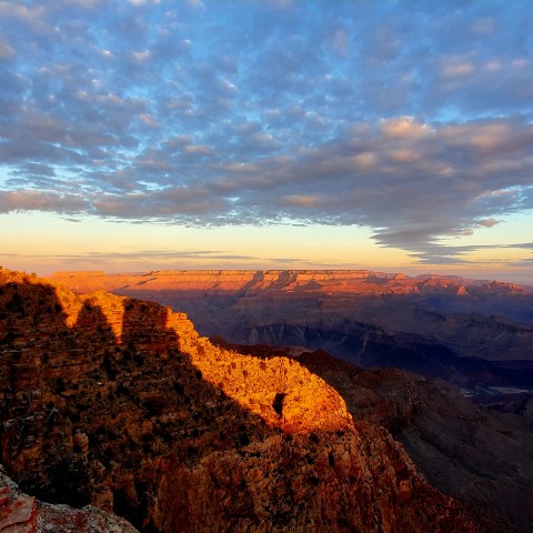 Sunset view of Grand Canyon with dramatic clouds and a watchtower on the left.