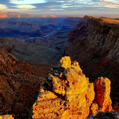Sunset over a vast canyon landscape with rocky cliffs and a distant river.