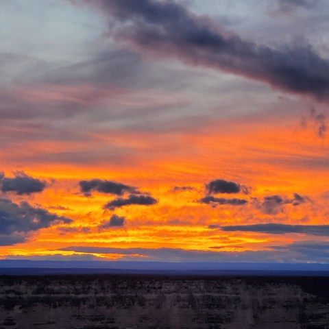 Vibrant sunset with orange clouds over a dark horizon.