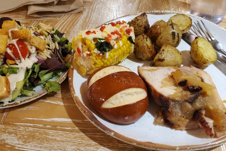 Plates of food with salad, roasted potatoes, corn, bread, and meat slice.