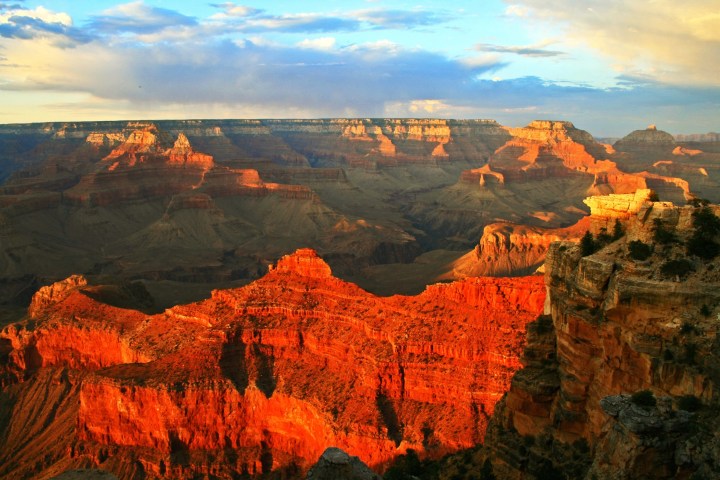 Sunset view of the Grand Canyon with red rock formations and a blue sky.