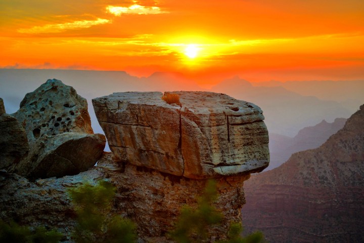 Rocky cliff at sunset with vivid orange sky and distant mountains.