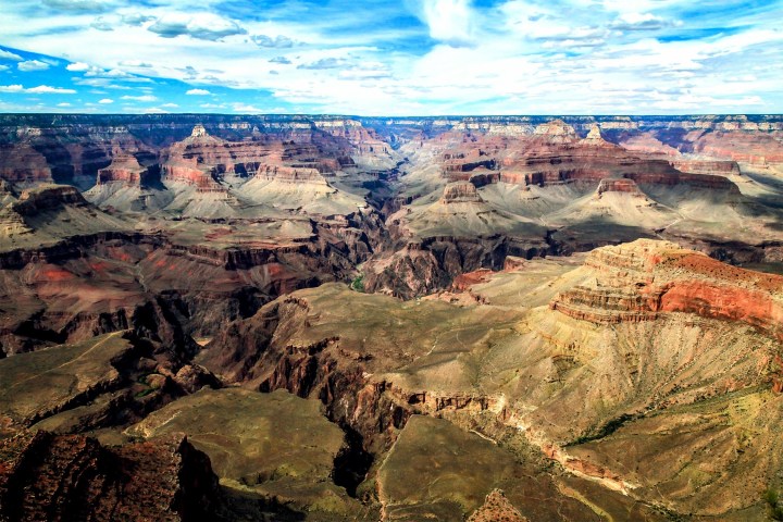 A panoramic view of the Grand Canyon under a blue sky with scattered clouds.