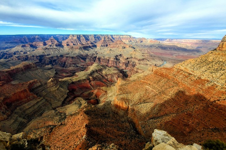 Vast view of Grand Canyon with layered rock formations under a cloudy sky.