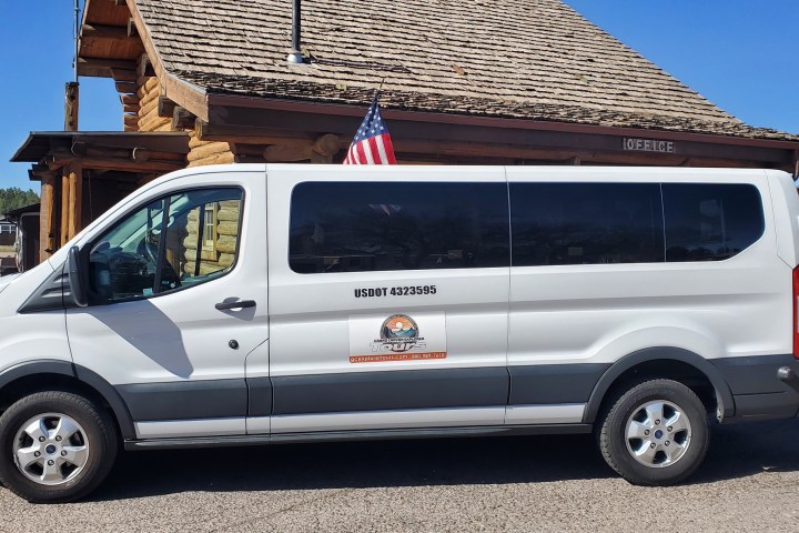 White van parked in front of a log cabin with an American flag.
