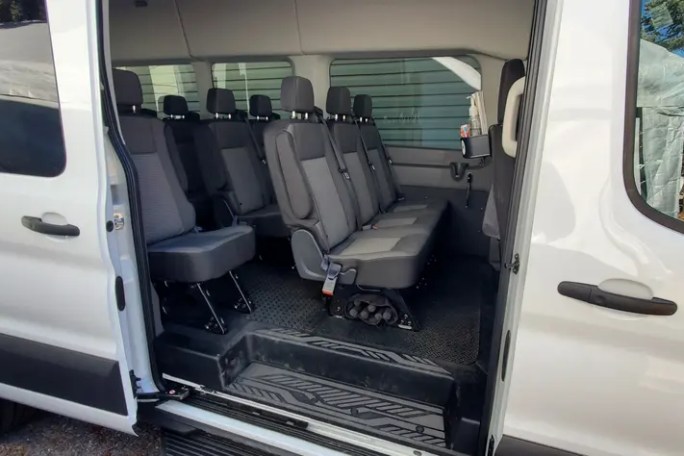 Open side door of a passenger van showing rows of gray seats.