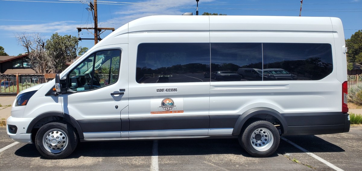 White passenger van with mountains logo parked in a lot.
