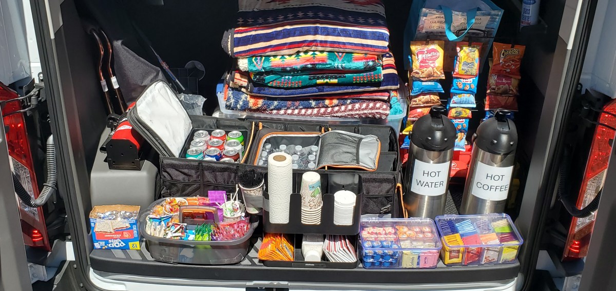 Van trunk with snacks, drinks, blankets, and coffee dispensers neatly arranged.