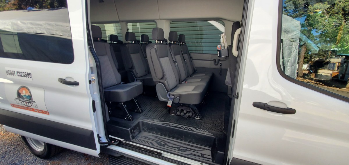 Open door view of a passenger van with multiple rows of gray seats.
